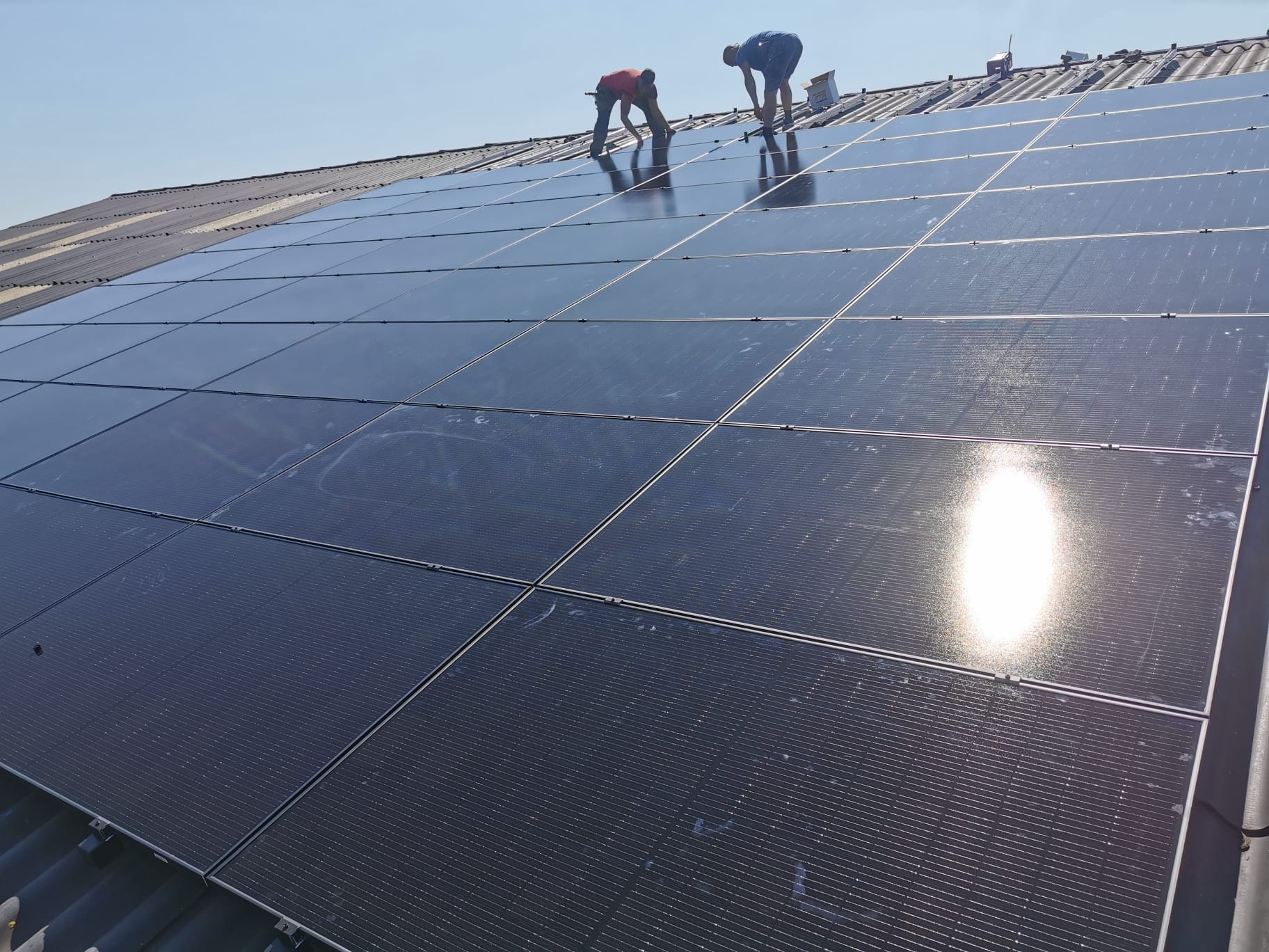 Solar panels on a sloping roof, with two people near the top row of panels.